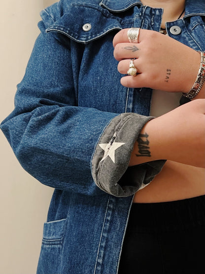 A close up image of a woman's hands wearing silver rings fixing the cuff of her jacket. The jacket has a star pattern inside.